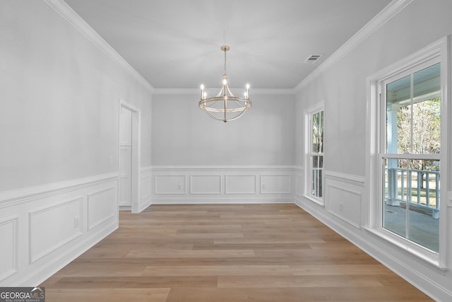 unfurnished dining area featuring visible vents, crown molding, light wood-style flooring, and an inviting chandelier