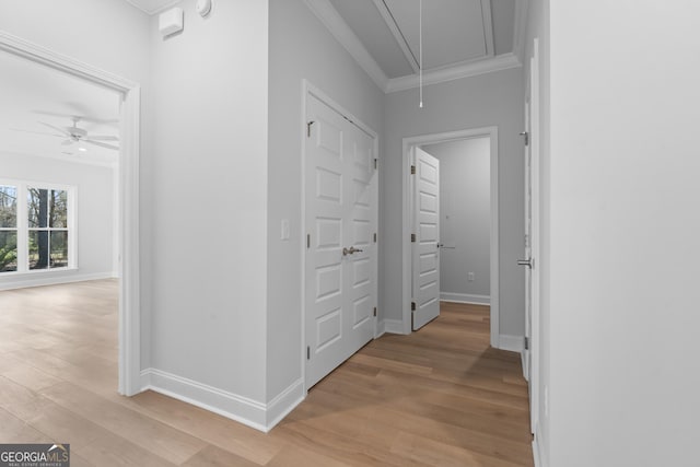 hall featuring ornamental molding, light wood-style flooring, attic access, and baseboards