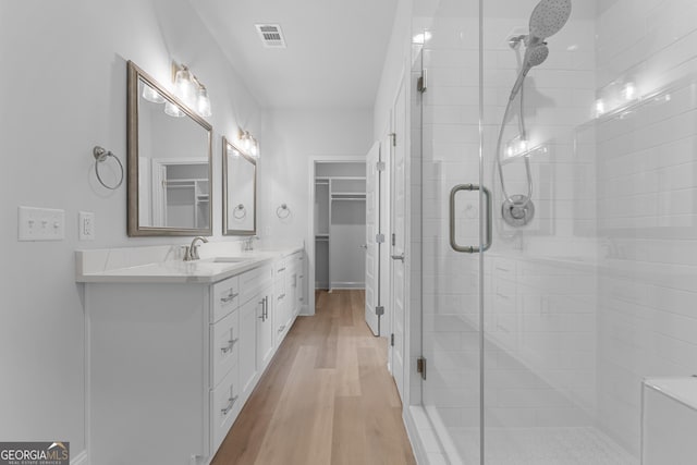 full bathroom with double vanity, visible vents, a stall shower, a sink, and wood finished floors