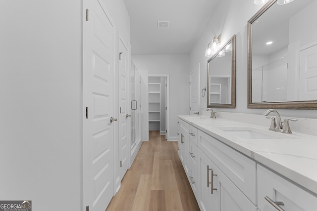 full bath featuring double vanity, wood finished floors, a sink, and visible vents