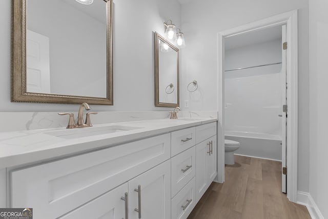 bathroom with double vanity, wood finished floors, a sink, and toilet