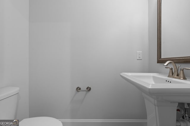 half bathroom featuring toilet, baseboards, and a sink