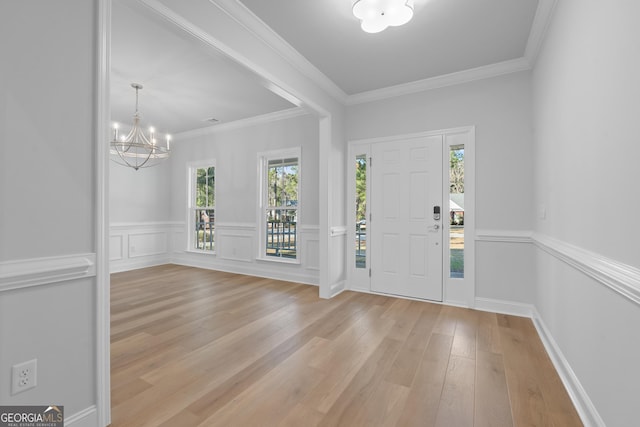 entrance foyer featuring a wainscoted wall, ornamental molding, an inviting chandelier, and light wood-style floors