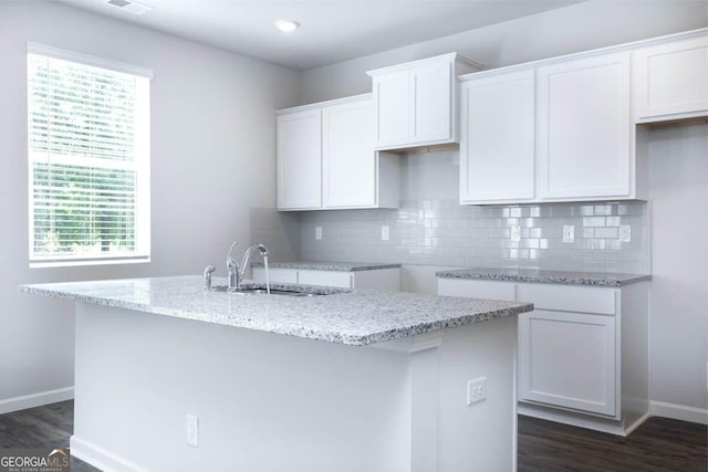 kitchen featuring dark wood-style flooring, a sink, white cabinetry, backsplash, and light stone countertops