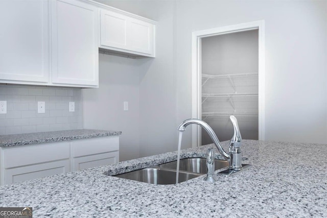 kitchen featuring light stone countertops, white cabinetry, decorative backsplash, and a sink