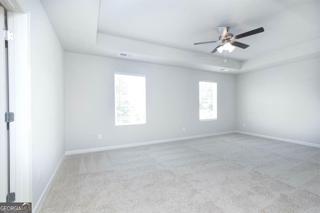 carpeted empty room featuring ceiling fan, a raised ceiling, visible vents, and baseboards