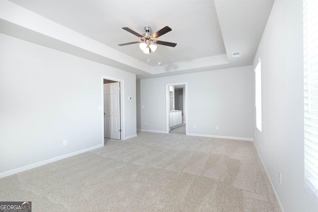 unfurnished bedroom with carpet floors, visible vents, baseboards, a raised ceiling, and ensuite bath