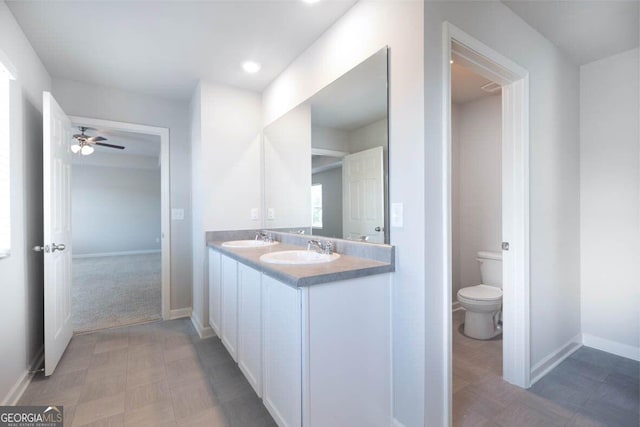 full bathroom with toilet, double vanity, baseboards, and a sink