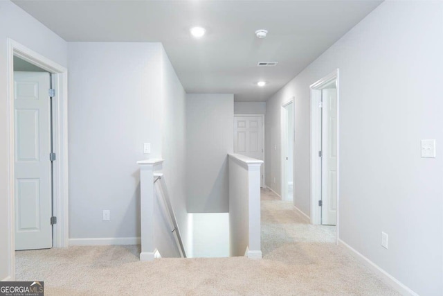 hallway with light carpet, visible vents, an upstairs landing, and baseboards