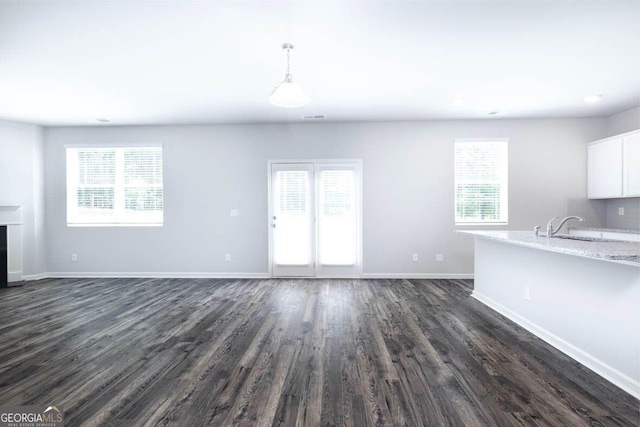 unfurnished living room with baseboards, dark wood finished floors, and a wealth of natural light