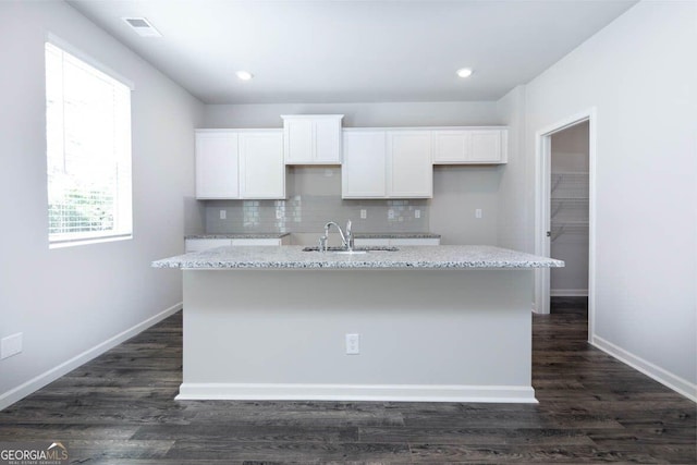 kitchen with decorative backsplash, white cabinets, a sink, an island with sink, and baseboards