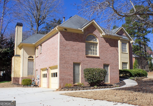 view of side of property featuring a garage, driveway, brick siding, and a chimney