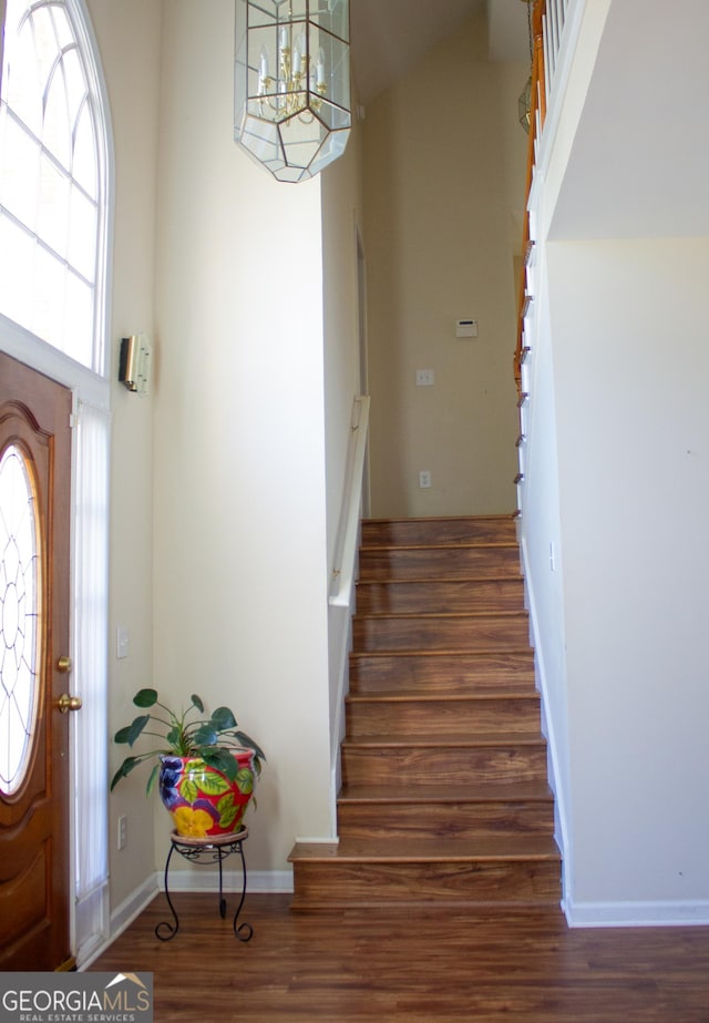 foyer featuring stairs, a notable chandelier, baseboards, and wood finished floors