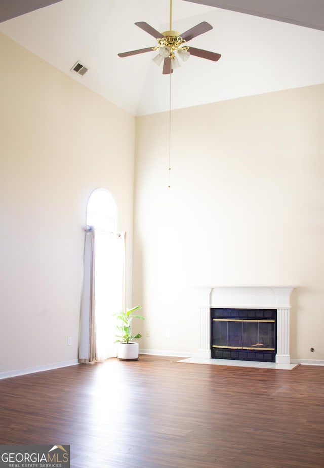 unfurnished living room with visible vents, baseboards, a fireplace with flush hearth, wood finished floors, and high vaulted ceiling