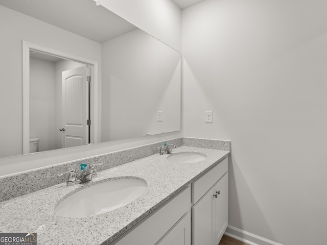 bathroom featuring toilet, a sink, baseboards, and double vanity