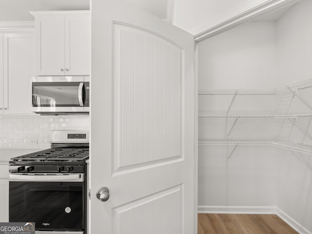 kitchen featuring tasteful backsplash, white cabinets, appliances with stainless steel finishes, light countertops, and light wood-type flooring