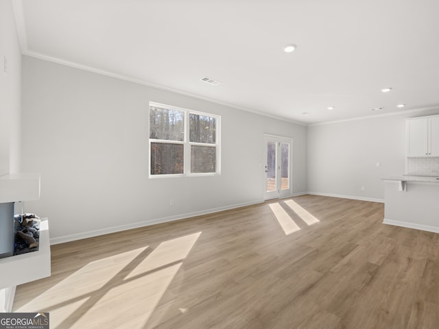 unfurnished living room featuring baseboards, ornamental molding, visible vents, and light wood-style floors