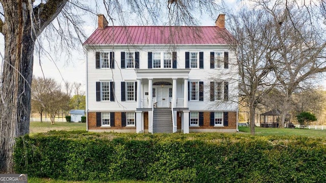 view of front of property with brick siding, metal roof, and a chimney