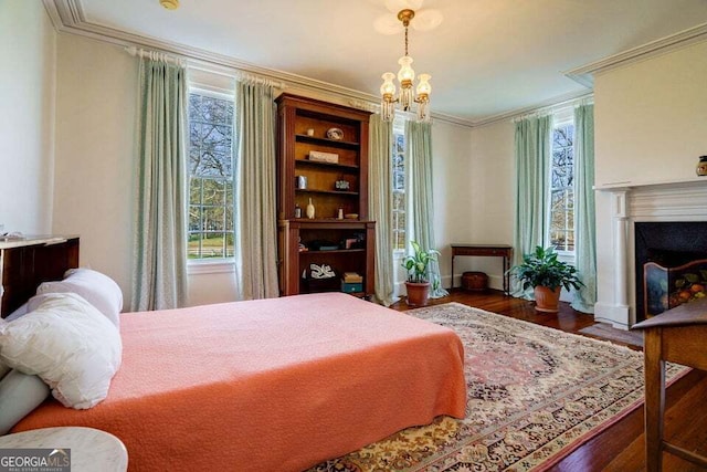 bedroom with a notable chandelier, a fireplace, ornamental molding, and wood finished floors