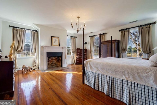 bedroom featuring wood-type flooring, a fireplace with flush hearth, visible vents, and a notable chandelier