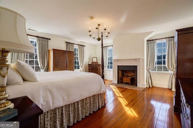 bedroom with hardwood / wood-style flooring, a fireplace with flush hearth, baseboards, and a notable chandelier