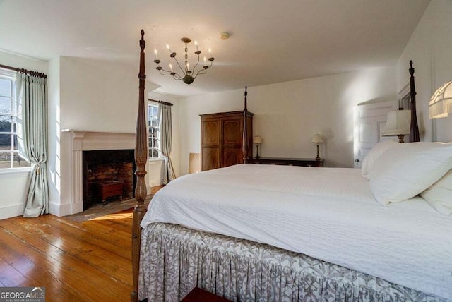 bedroom with a chandelier, wood-type flooring, a fireplace, and baseboards