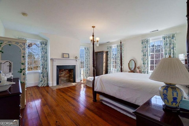 bedroom with hardwood / wood-style flooring, a fireplace with flush hearth, visible vents, and a notable chandelier