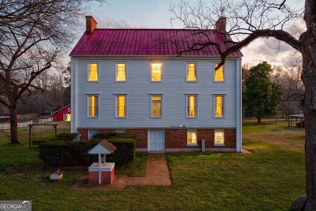 view of front of property with metal roof, brick siding, a yard, and a chimney