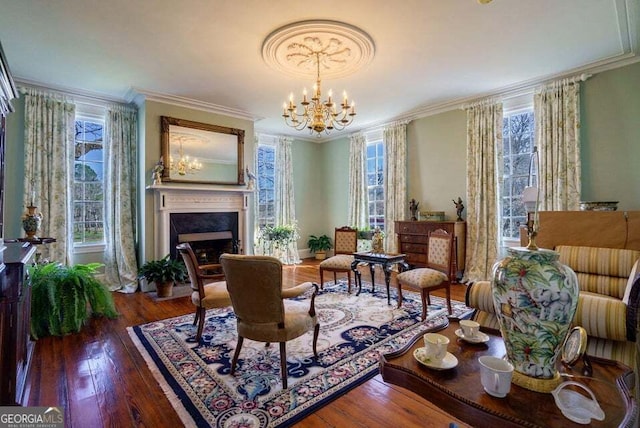 living area featuring crown molding, wood-type flooring, a fireplace, and an inviting chandelier