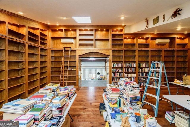 interior space with a wall mounted AC, wall of books, and wood finished floors