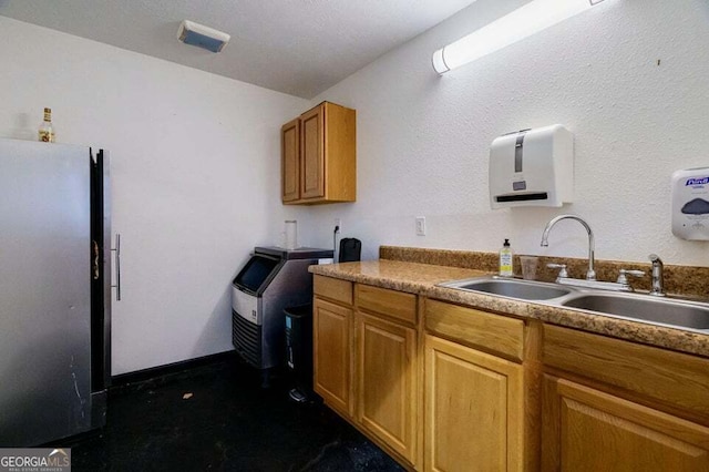 kitchen featuring brown cabinetry, a sink, and freestanding refrigerator