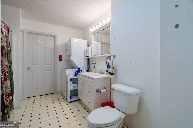 full bathroom featuring toilet, stacked washing maching and dryer, a textured ceiling, and vanity