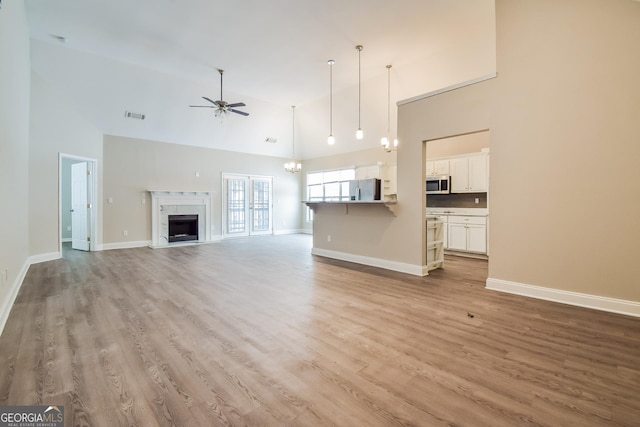 unfurnished living room with ceiling fan with notable chandelier, baseboards, and light wood-style floors