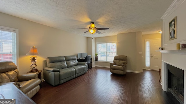 living room with baseboards, ceiling fan, dark wood-type flooring, a textured ceiling, and a fireplace