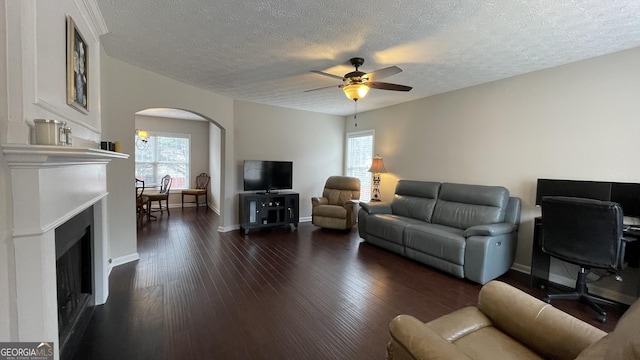 living room featuring arched walkways, a fireplace, dark wood-style floors, and a ceiling fan