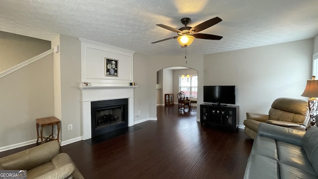 living room with dark wood-type flooring, arched walkways, ceiling fan, and a textured ceiling