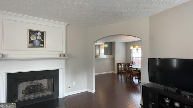 living room with dark wood-type flooring, arched walkways, a fireplace with raised hearth, and a textured ceiling