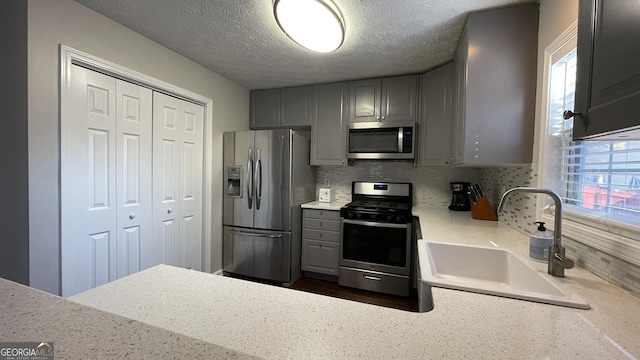 kitchen featuring gray cabinets, light countertops, appliances with stainless steel finishes, a healthy amount of sunlight, and a sink