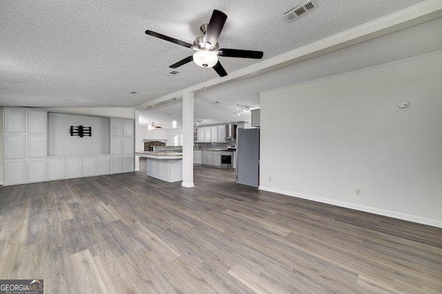 unfurnished living room featuring visible vents, vaulted ceiling, a textured ceiling, wood finished floors, and baseboards