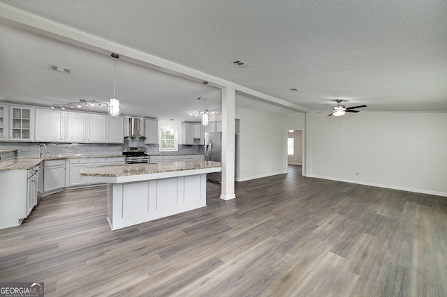 kitchen featuring lofted ceiling, wall chimney exhaust hood, wood finished floors, stainless steel appliances, and backsplash