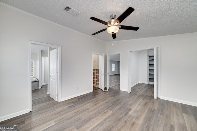 unfurnished bedroom featuring visible vents, ornamental molding, a textured ceiling, wood finished floors, and baseboards