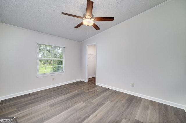 spare room featuring a textured ceiling, ornamental molding, wood finished floors, and baseboards