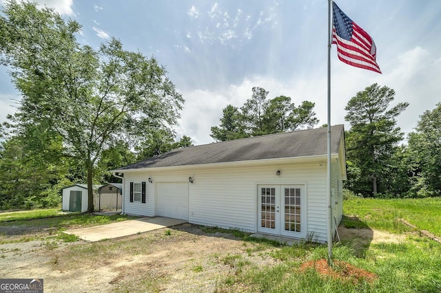 exterior space with a garage, an outdoor structure, dirt driveway, french doors, and a storage unit