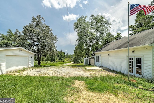 view of yard featuring a detached garage, an outbuilding, and french doors