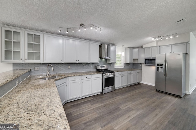 kitchen with dark wood finished floors, decorative backsplash, appliances with stainless steel finishes, a sink, and wall chimney exhaust hood