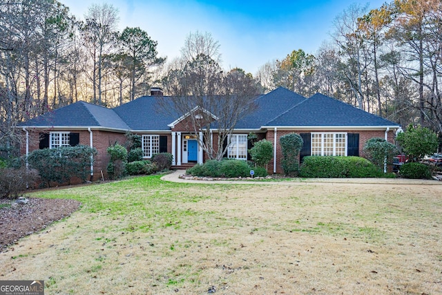 ranch-style house with brick siding, a chimney, and a front yard