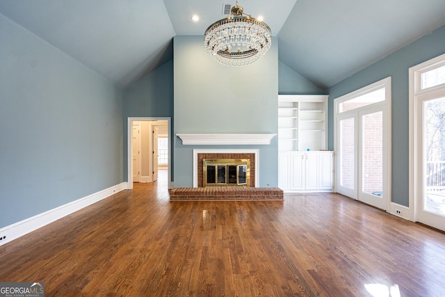 unfurnished living room featuring a fireplace, visible vents, an inviting chandelier, wood finished floors, and baseboards