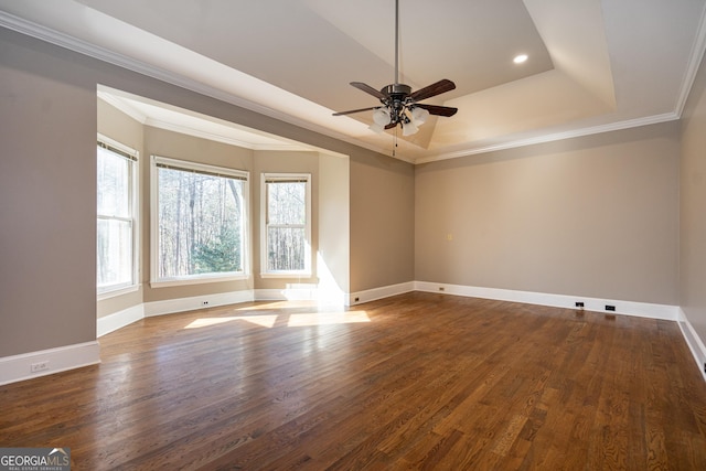 empty room with dark wood-type flooring, a tray ceiling, ornamental molding, and baseboards