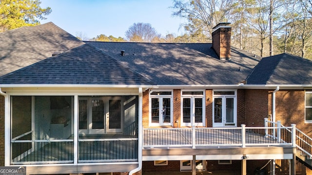 rear view of house with brick siding, a sunroom, roof with shingles, a wooden deck, and a chimney