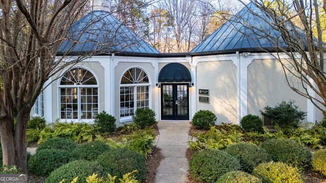 view of exterior entry featuring french doors, metal roof, a standing seam roof, and stucco siding